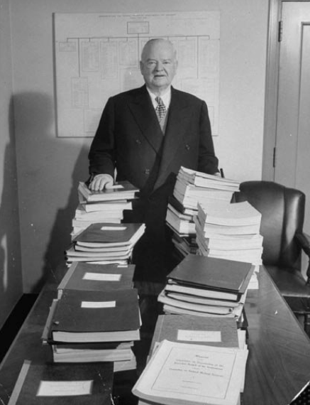 Former President Herbert C. Hoover, in 1949, standing in back of stacks of reports for Hoover Commission Studies. 
